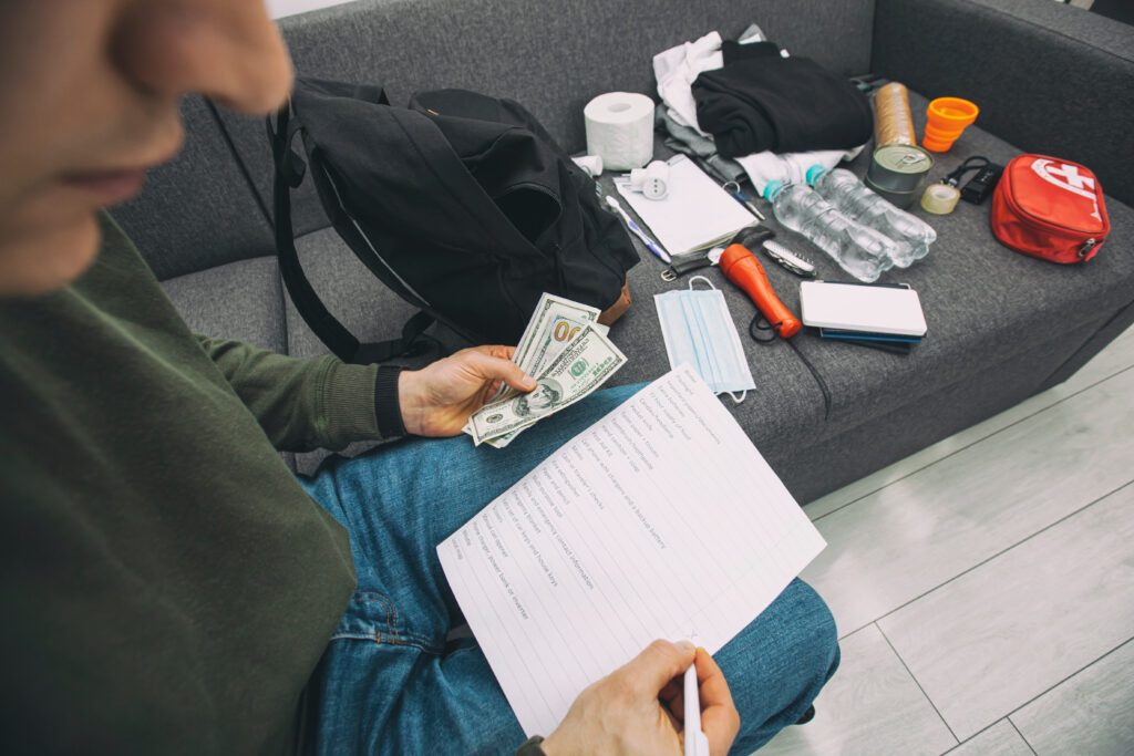 Young man packing the bag with documents, water,food, first aid kit and other items needed to surviveLe sac d'évacuation - NATUR'O TOP